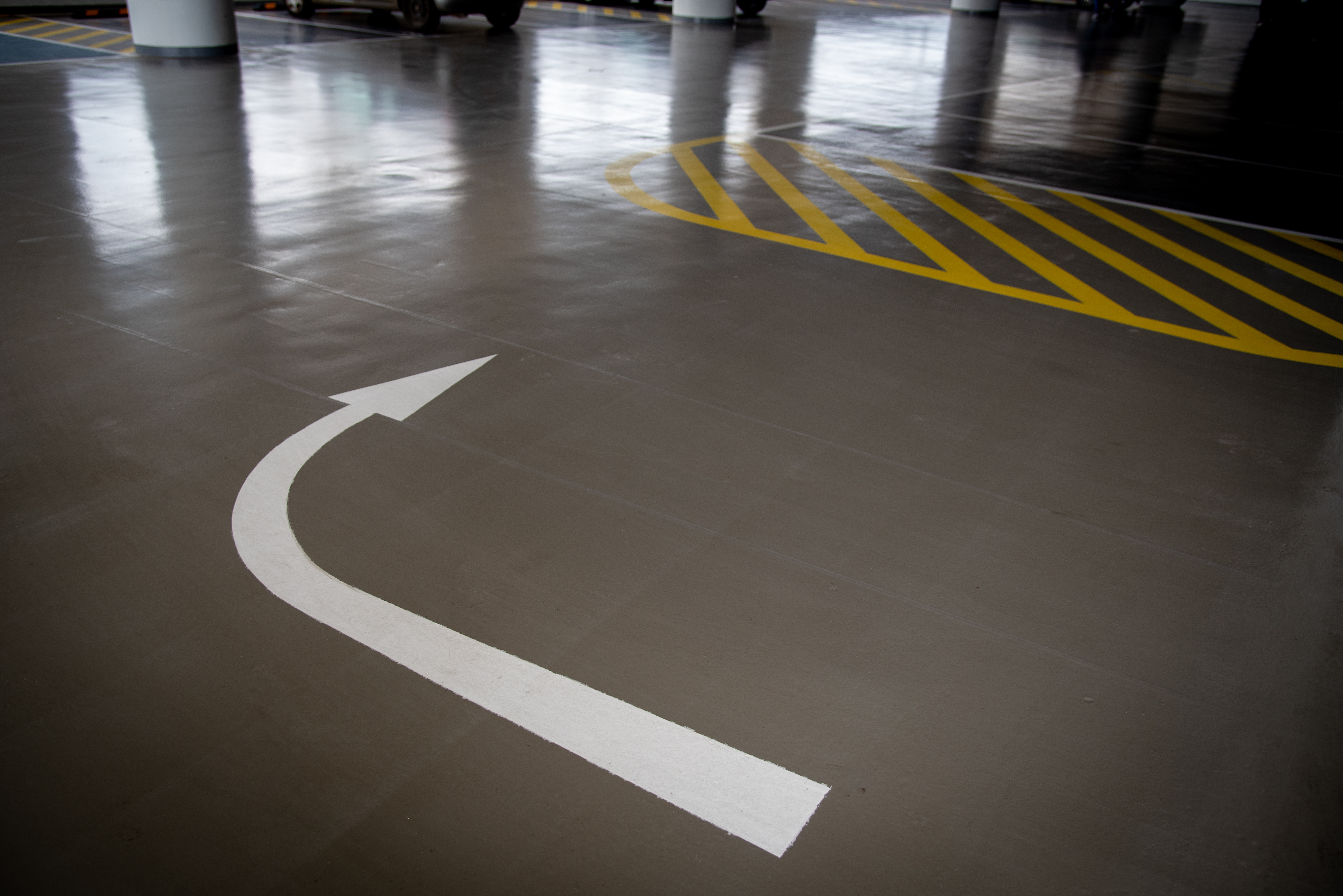 Coated commercial parking garage floor with painted directional arrows — the same high-build systems used in commercial garages are available for residential