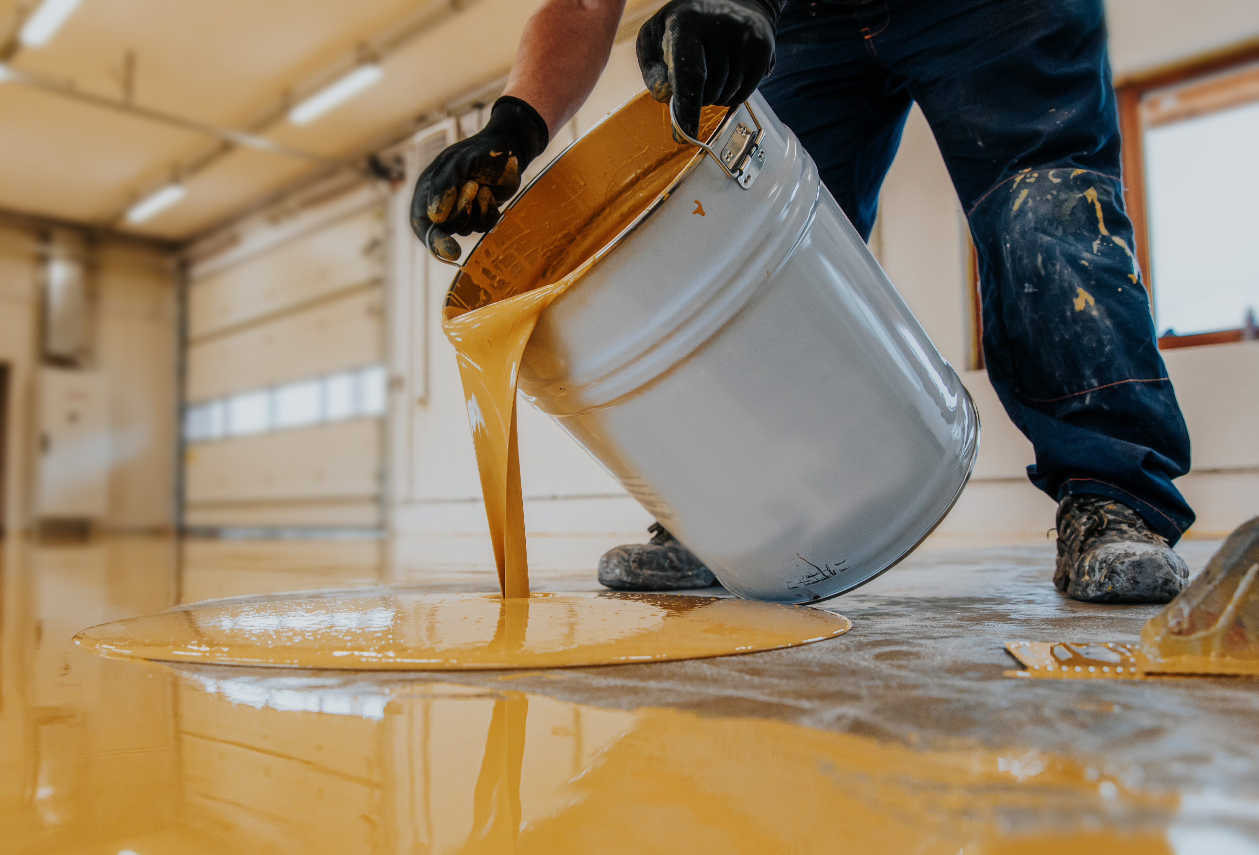 Industrial worker pouring epoxy floor coating in a garage — professional garage floor paint application